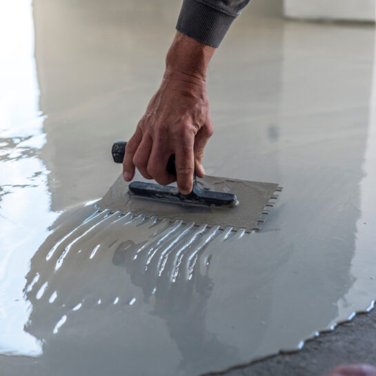 Grey self-leveling screed, new floor layer, man hand. Construction workers are painting the floor using the method self-leveling epoxy.spreading self leveling compound with trowel.Self-leveling epoxy. Leveling with a mixture of cement floors.